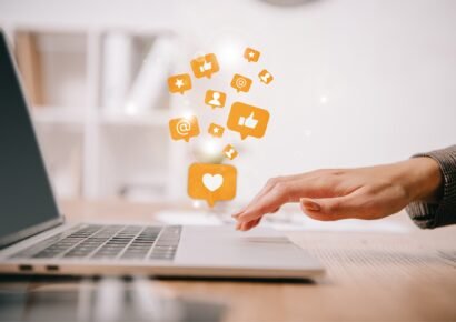 cropped view of businesswoman typing on laptop at workplace with multimedia icons