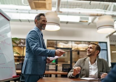 Mature business coach or speaker make flip chart presentation to diverse businesspeople at meeting