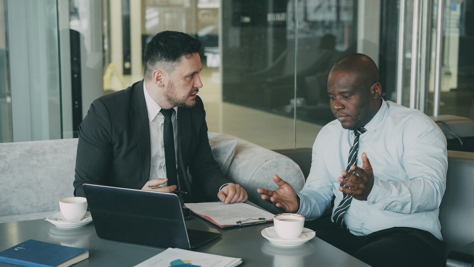 Confrontation Two businessmen discussing documents at a table.