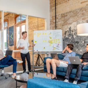 marketing three men sitting while using laptops and watching man beside whiteboard