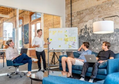 marketing three men sitting while using laptops and watching man beside whiteboard