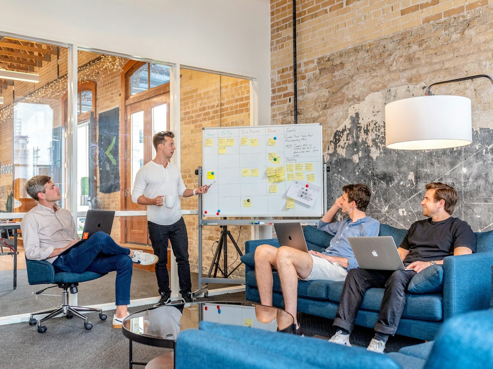Agile three men sitting while using laptops and watching man beside whiteboard